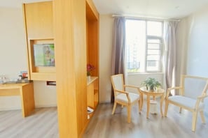 Ein Zimmer mit Schreibtisch aus Holz, zwei Stühlen, einem kleinen Tisch mit Pflanze und einem Fenster mit Vorhängen.