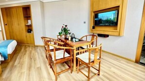A room with a wooden dining table and chairs, a TV mounted on the wall, and a bed with a blue blanket.