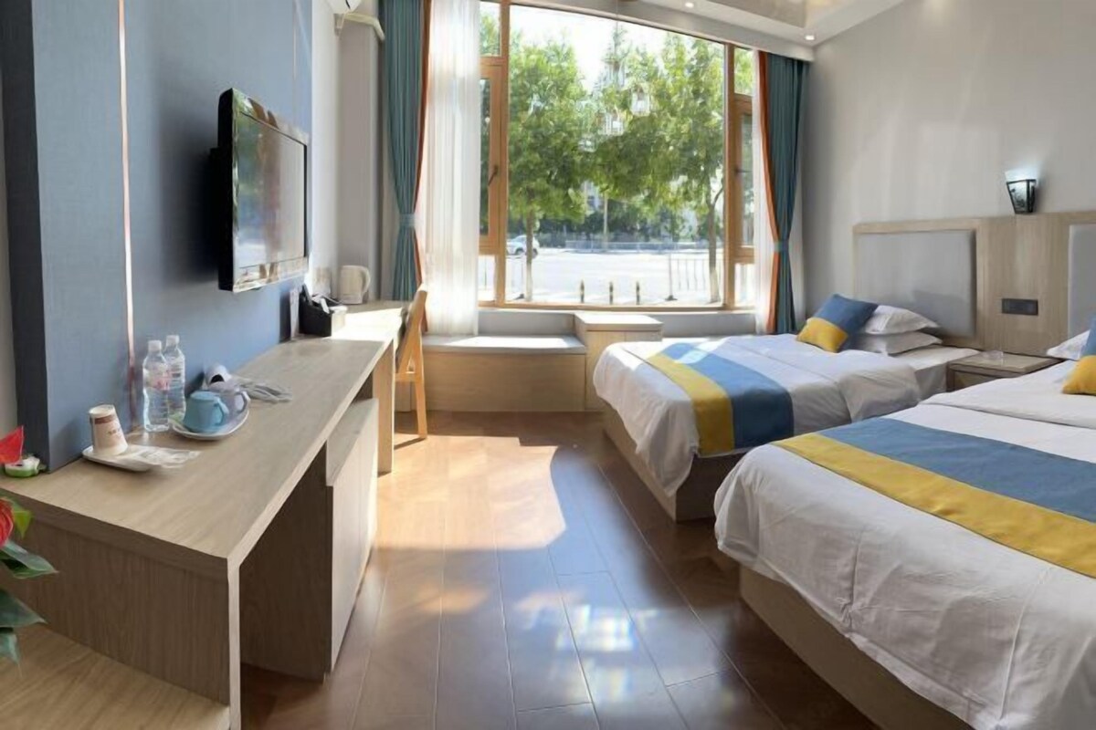 Ein Hotelzimmer mit Schreibtisch, zwei Betten, Fernseher und Fenster mit Blick auf die Straße.
