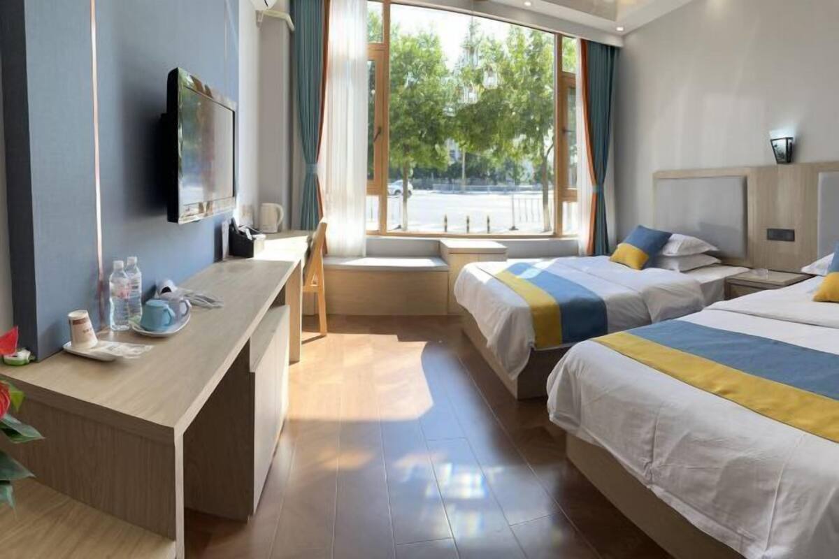 Ein Hotelzimmer mit Schreibtisch, zwei Betten, Fernseher und Fenster mit Blick auf die Straße.