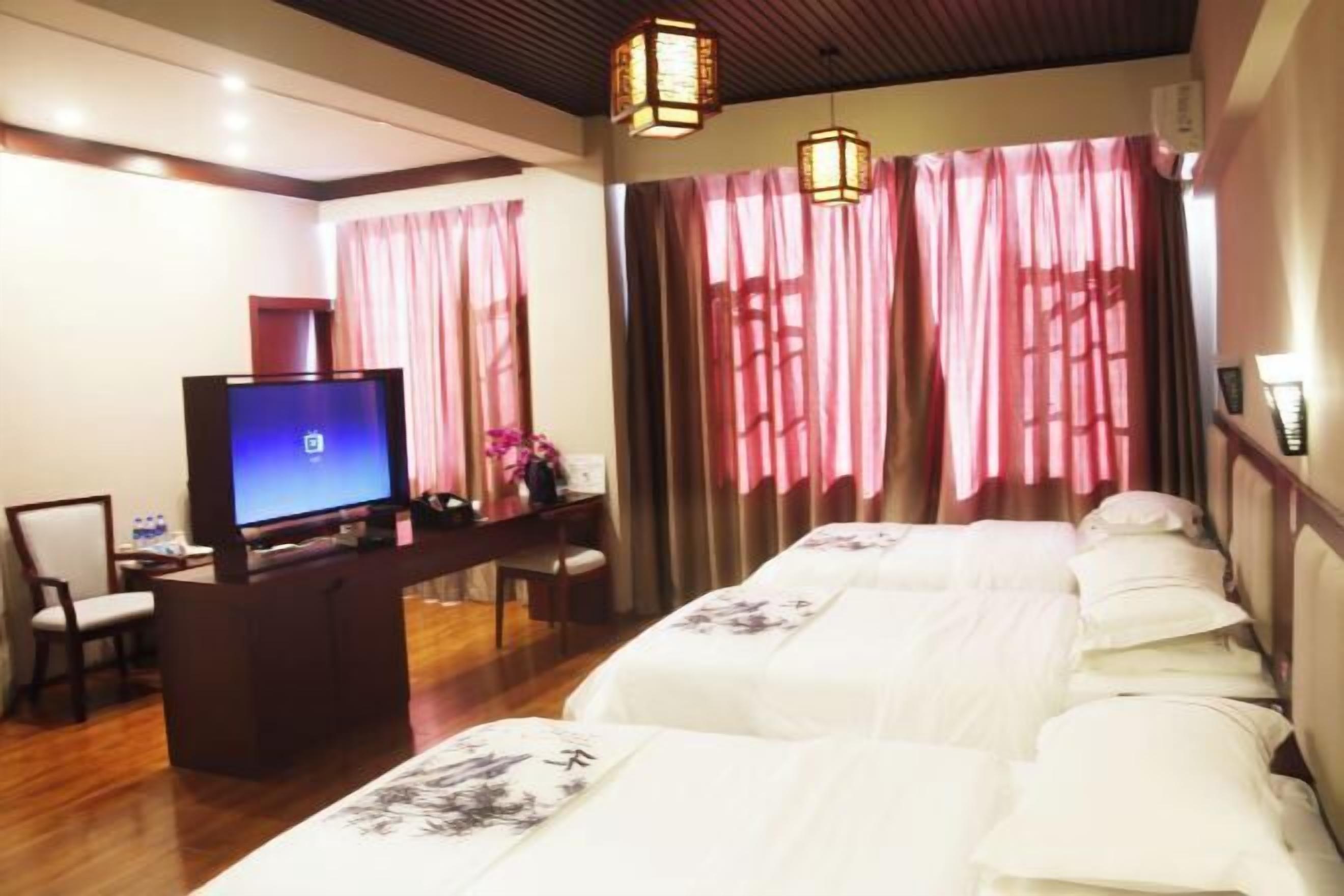 Habitación de hotel con televisión, escritorio, silla y cama con ropa de cama estampada.