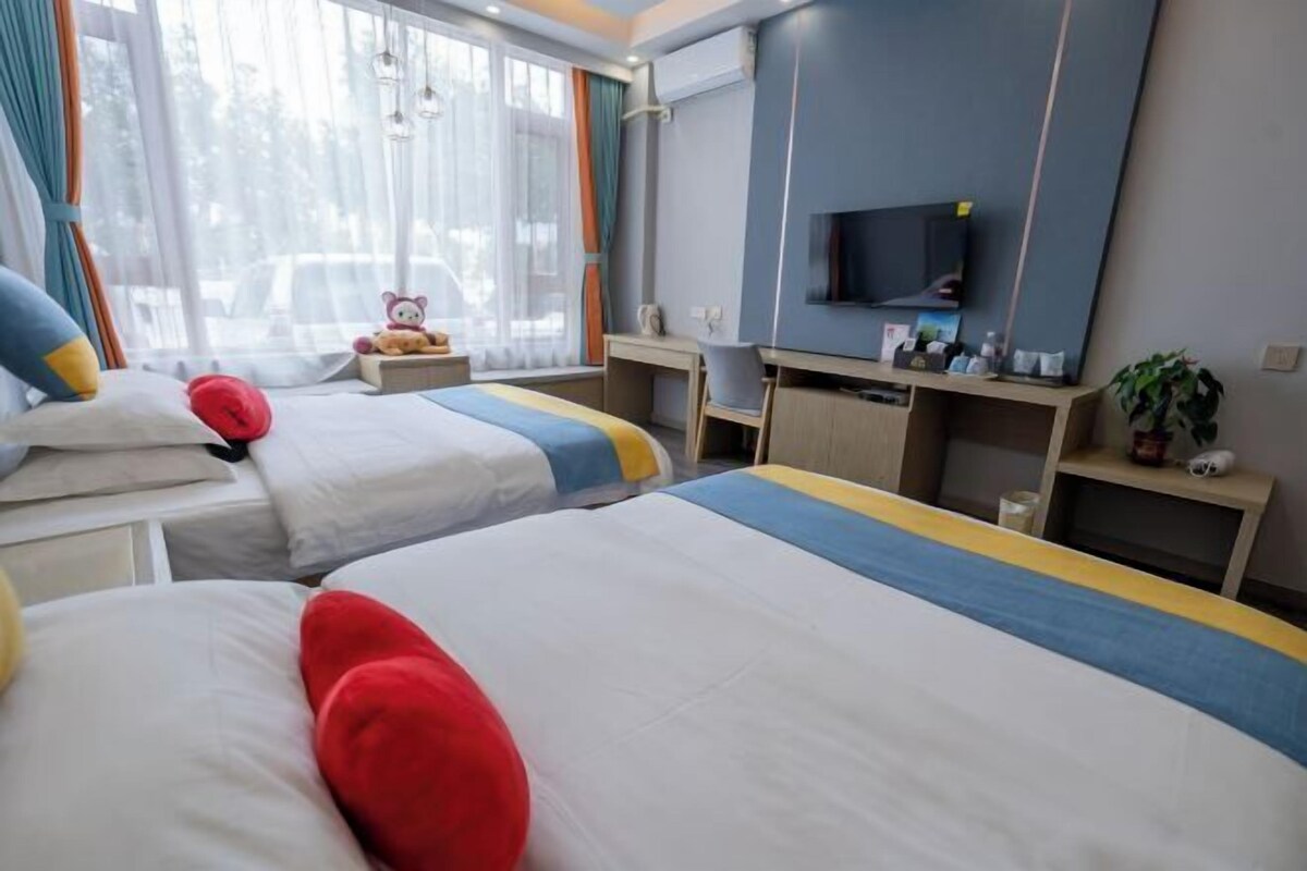 Ein Hotelzimmer mit zwei Betten, einem Schreibtisch, einem Fernseher und einem Fenster mit Vorhängen.