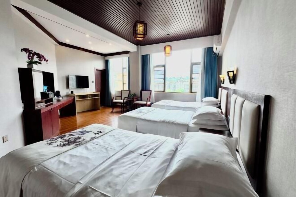 Ein Hotelzimmer mit zwei Betten, einem Schreibtisch, einem Fernseher und einem Vorhangfenster.