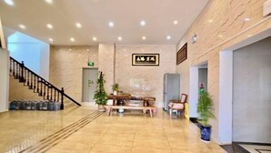 A lobby with a marble floor, a staircase, a reception desk, and potted plants.