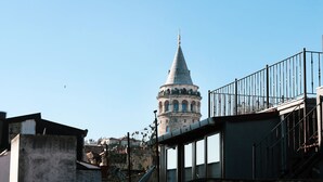 A view of a historic tower with a conical roof, surrounded by urban buildings and a metal fence. - Galata Masterpiece Hotel (Istanbul)