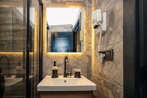 Un baño moderno con un espejo grande, un lavamanos con grifo y un secador de pelo montado en la pared.