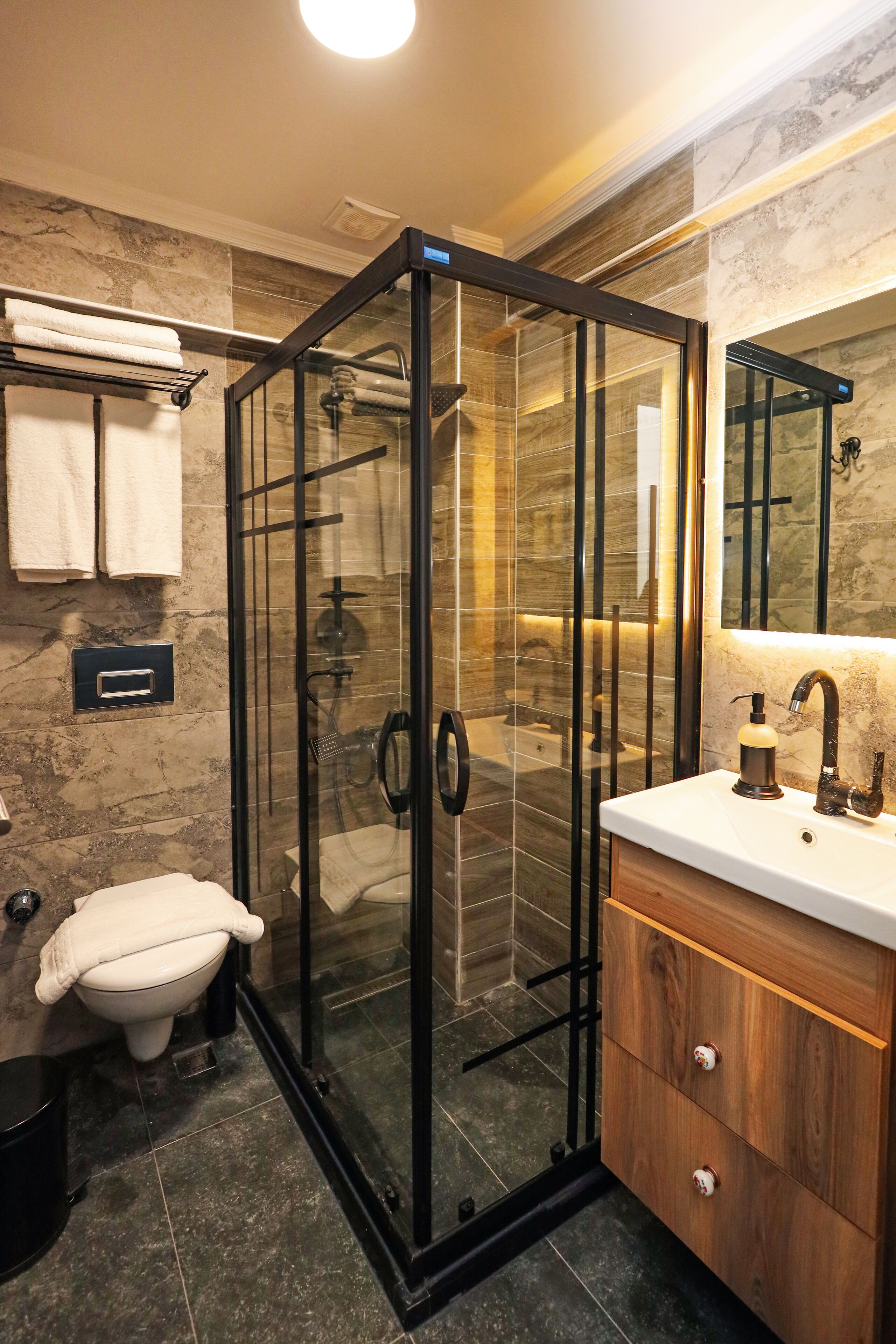 Un baño moderno con ducha cubierta por vidrio, inodoro blanco y tocador de madera con espejo.