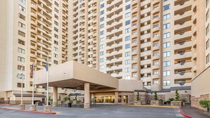 Un hôtel de grande hauteur avec une entrée centrale, de nombreux balcons et un espace de stationnement.