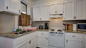 Une cuisine avec des meubles blancs, une cuisinière, un évier et une fenêtre avec un rideau.