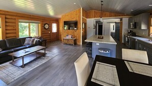 Amplio salón con sofá, mesa de centro y zona de comedor. Se ve una cocina con electrodomésticos modernos y una isla grande.