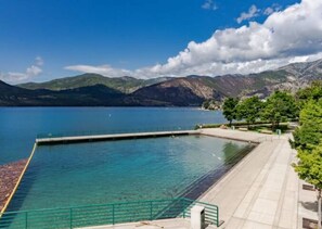A swimming pool with clear blue water, surrounded by a paved walkway and greenery, overlooking a mountainous landscape.
