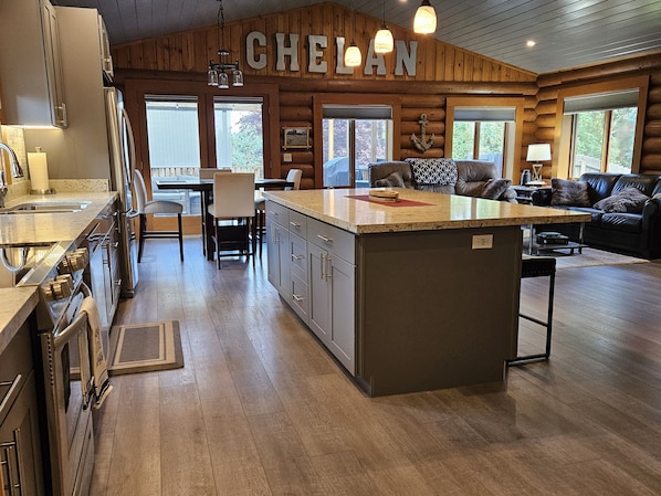 A spacious kitchen with a large island, wooden cabinetry, and a dining area with a view of the outdoors.