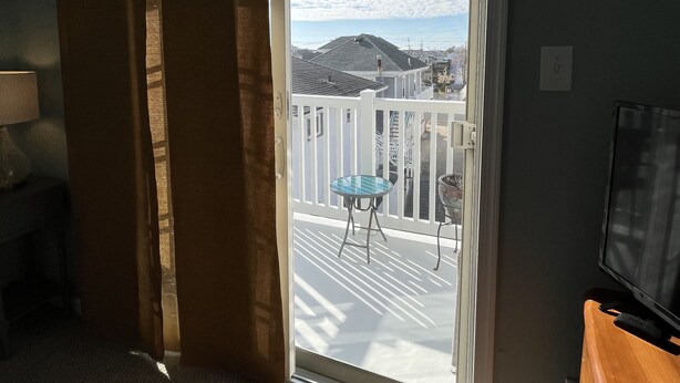 Een kamer met een schuifpui die leidt naar een balkon met een witte reling en een klein tafeltje.