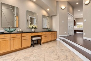 A bathroom with a vanity, a glass bowl sink, and a bench.