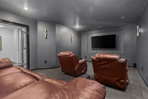 Habitación con una televisión de pantalla plana grande montada en la pared, dos sillones de cuero y una cama grande.