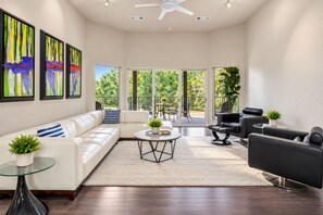 A spacious living room with a white sofa, black leather chairs, a glass coffee table, and a large window offering a view of greenery. - McKenzie Cove - Private dock & lake views (Hot Springs)