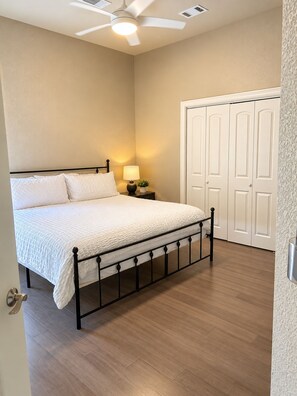 A bedroom with a bed, a nightstand with a lamp, a ceiling fan, and a set of white doors.