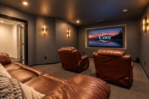 A home theater room with leather reclining chairs, a large flat-screen TV, and wall-mounted lighting.