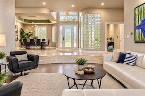 A modern living room with a curved sofa, a coffee table, and a dining area with a table and chairs. - McKenzie Cove - Private dock & lake views (Hot Springs)