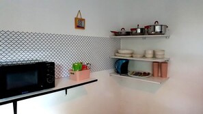 Eine Küche mit einer Mikrowelle, Regalen mit Töpfen und Schüsseln sowie einem Wandbild.