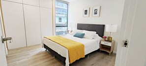 Ein Schlafzimmer mit Bett, Nachttisch, Lampe und einem Kunstwerk an der Wand.
