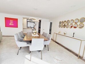 A modern dining area with a wooden table and grey upholstered chairs, a kitchen in the background, and a wall with circular mirrors.