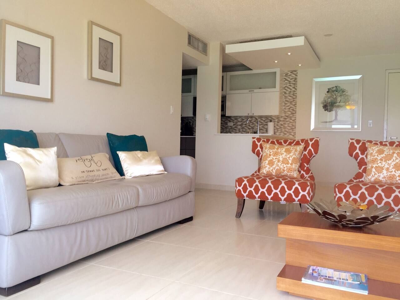 Una sala de estar con un sofá, dos sillones, una mesita de centro y una cocina al fondo.