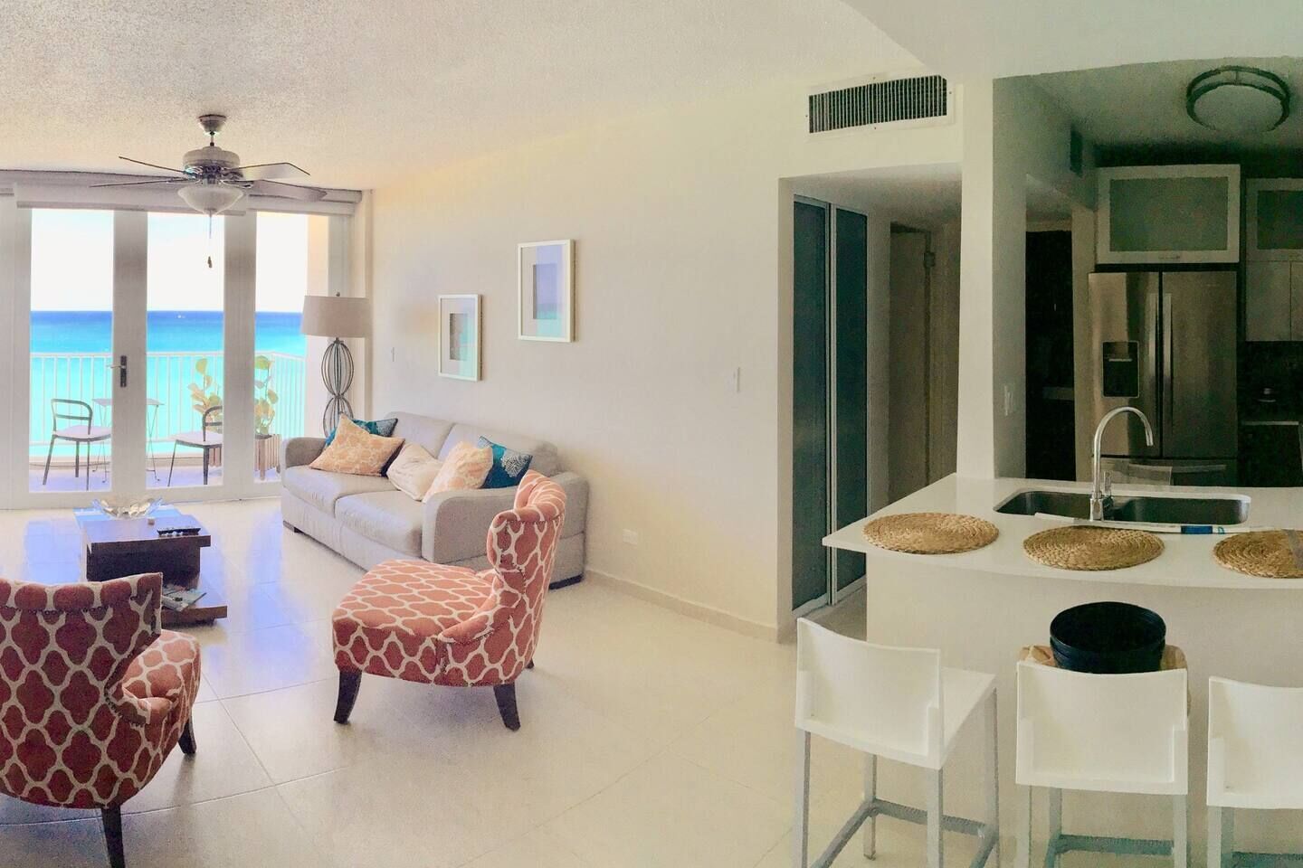 Un salon moderne comprenant un canapé, un fauteuil à motifs de girafe, un coin repas avec une table blanche et une cuisine dotée d’un grand réfrigérateur et d’un évier.