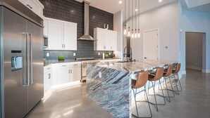 A modern kitchen with a marble island, stainless steel appliances, and a black hexagonal backsplash.