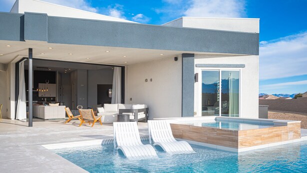 A modern house with an infinity pool, outdoor seating, and a view of the mountains.