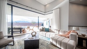 A modern living room with a sofa, coffee table, and a view of a pool and mountains.
