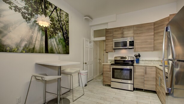 Une cuisine moderne avec des meubles en bois, des appareils en acier inoxydable, un plan de travail blanc et un tableau représentant une scène de forêt.