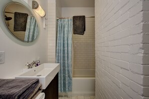 A bathroom with a white sink, a mirror, a towel rack with towels, a shower curtain, and a bathtub.
