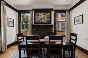 A dining area with a fireplace, wooden chairs, a table with a floral tablecloth, and framed artwork on the walls. - Boise-Downtown-historical-unique Arthouse 2 (Boise)