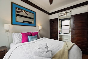 A hotel room with a bed, pillows, a bedside lamp, a mirror, a ceiling fan, and a wardrobe.