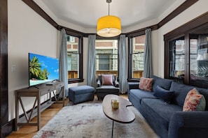 A living room with a television, sofa, ottoman, and a coffee table.