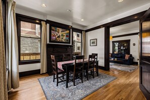 A dining area with a table set for six, flanked by wooden chairs, a patterned rug, and a large painting above the table.