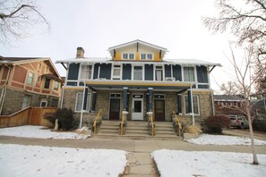A two-story building with a front entrance, a set of stairs, and a snow-covered ground.