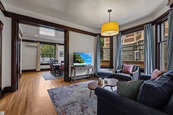 A modern living room with a flat-screen TV, a sofa, a coffee table, and a dining area with a table and chairs.