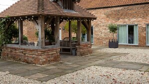 A gazebo with a brick base and wooden beams, a brick building with a tiled roof in the background, and a gravel ground. - Manor House (York)