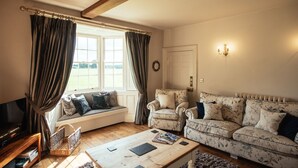A cozy living room with a wooden coffee table, two floral-patterned sofas, a television, and a window with curtains. - Manor House (York)