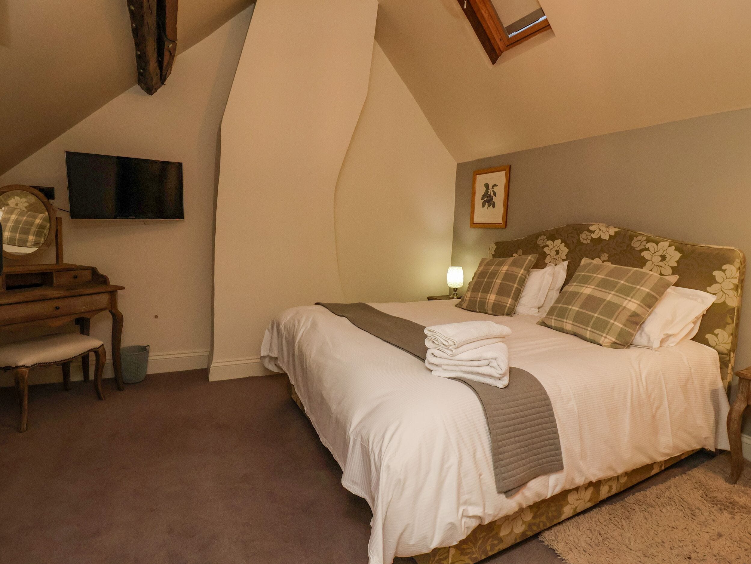 Een slaapkamer met een bed, bureau, stoel, televisie en een lijst aan de muur.
