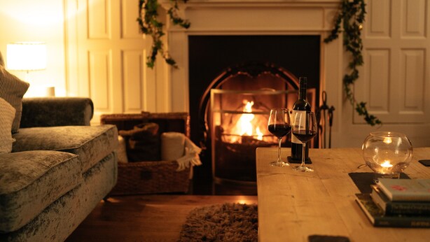 A cozy living room with a fireplace, a sofa, a coffee table with books and glasses, and a lamp. - Manor House (York)