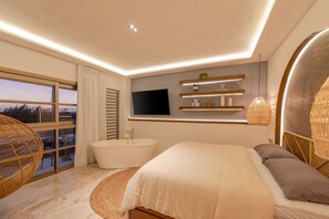 Een moderne slaapkamer met een groot bed, een badkuip, een aan de muur bevestigde televisie en uitzicht op de omgeving door grote ramen.
