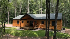 A log cabin with a porch, surrounded by a forest.