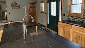 A kitchen with a black countertop, a stainless steel sink, wooden cabinets, a green door, and a welcome sign.