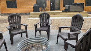 A log cabin with a patio area featuring three Adirondack chairs and a metal fire pit.