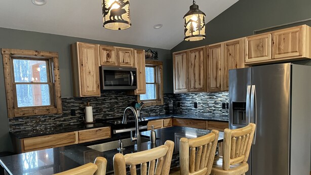 A modern kitchen with wooden cabinets, a stainless steel refrigerator, and a large island with bar stools.