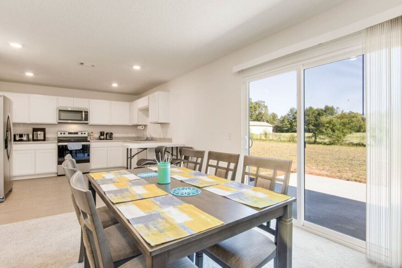 Una cocina moderna con armarios blancos, un microondas y un comedor con una mesa dispuesta para cuatro.