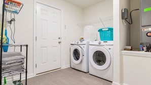 A laundry room with two front-loading washing machines, a drying rack, and a metal rack with folded towels.
